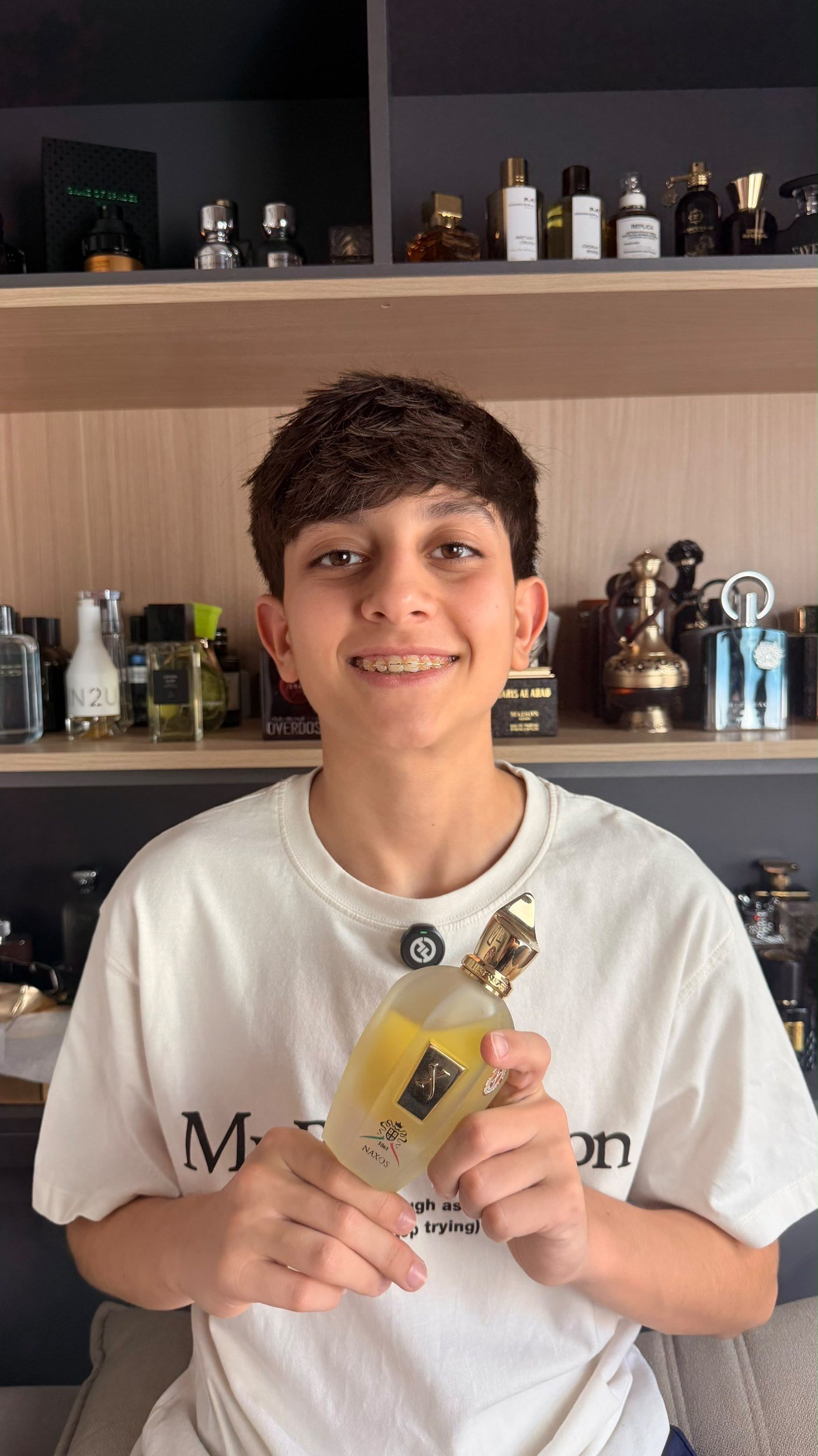 Rafael sorrindo, com um perfume Xerjoff Naxos em frente à sua coleção